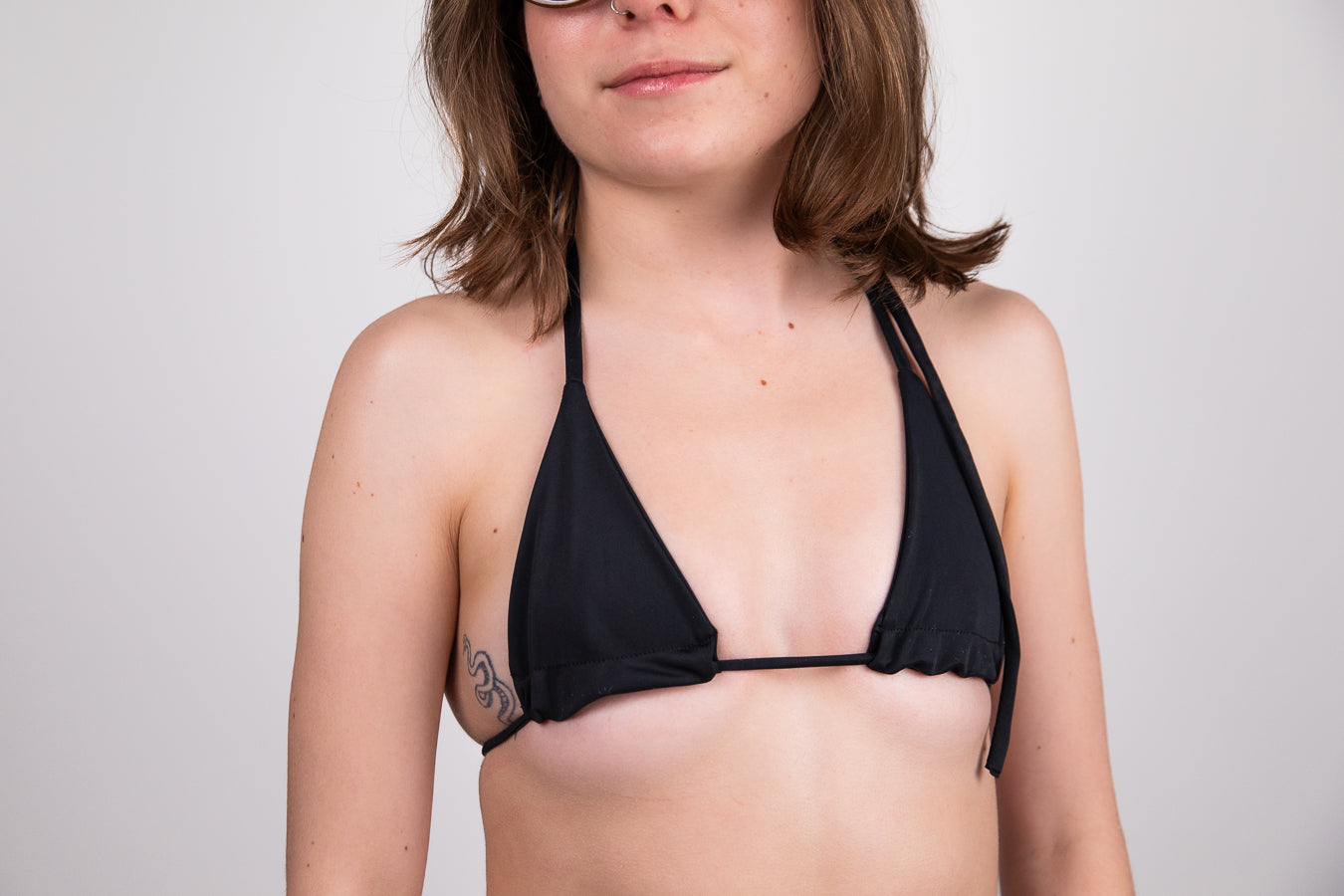 Person wearing a black bikini top against a plain background